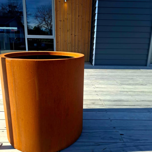 Handcrafted round steel planter in a rust finish, styled with ornamental grasses on a modern patio – durable and weather-resistant, made in New Zealand