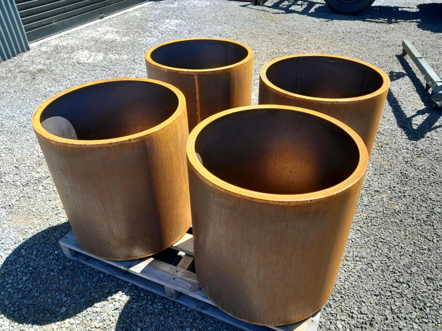 Handcrafted round steel planter in a rust finish, styled with ornamental grasses on a modern patio – durable and weather-resistant, made in New Zealand