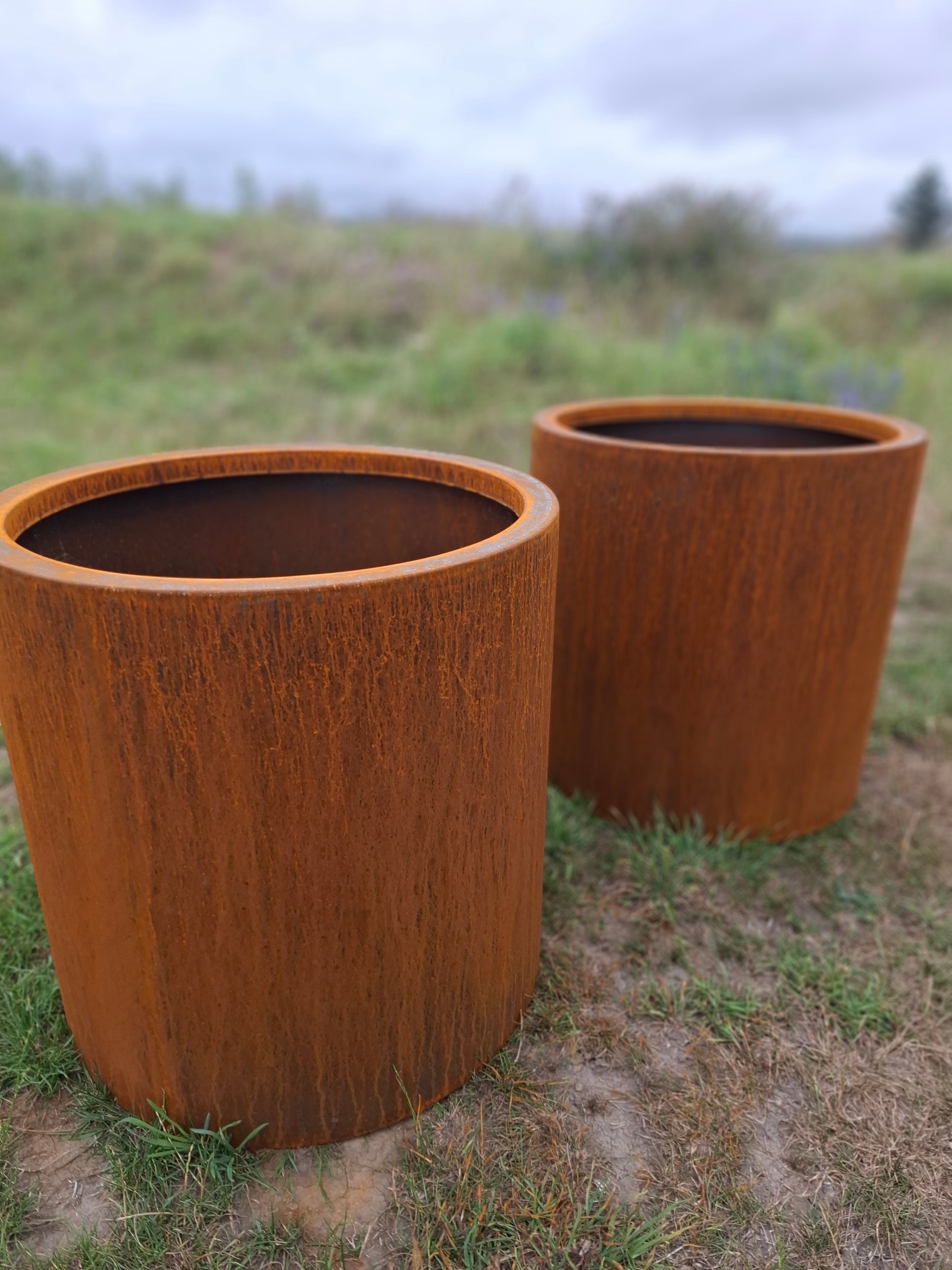 Handcrafted round steel planter in a rust finish, styled with ornamental grasses on a modern patio – durable and weather-resistant, made in New Zealand