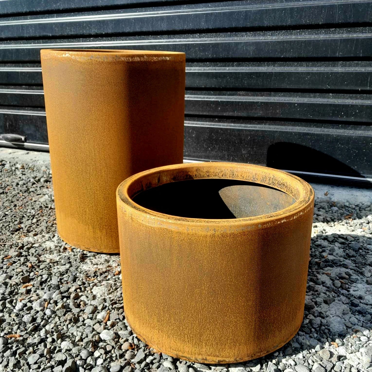 Handcrafted round steel planter in a rust finish, styled with ornamental grasses on a modern patio – durable and weather-resistant, made in New Zealand