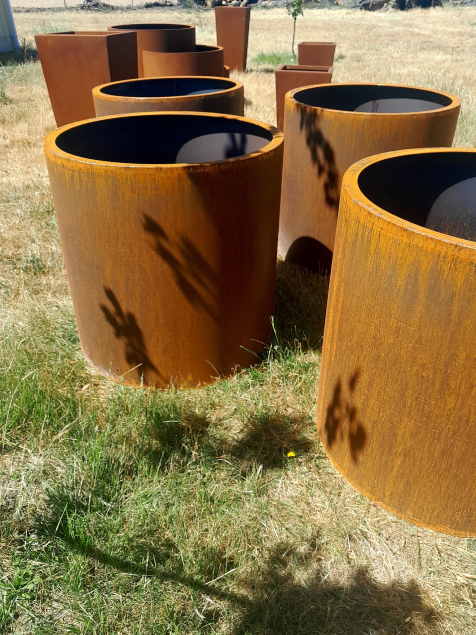 Handcrafted round steel planter in a rust finish, styled with ornamental grasses on a modern patio – durable and weather-resistant, made in New Zealand